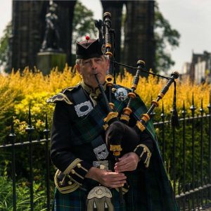 a man plays the bagpipes in front of the scott monument edinburgh