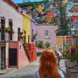 a woman looks up at the colourful buildings on a hill in guanajuato
